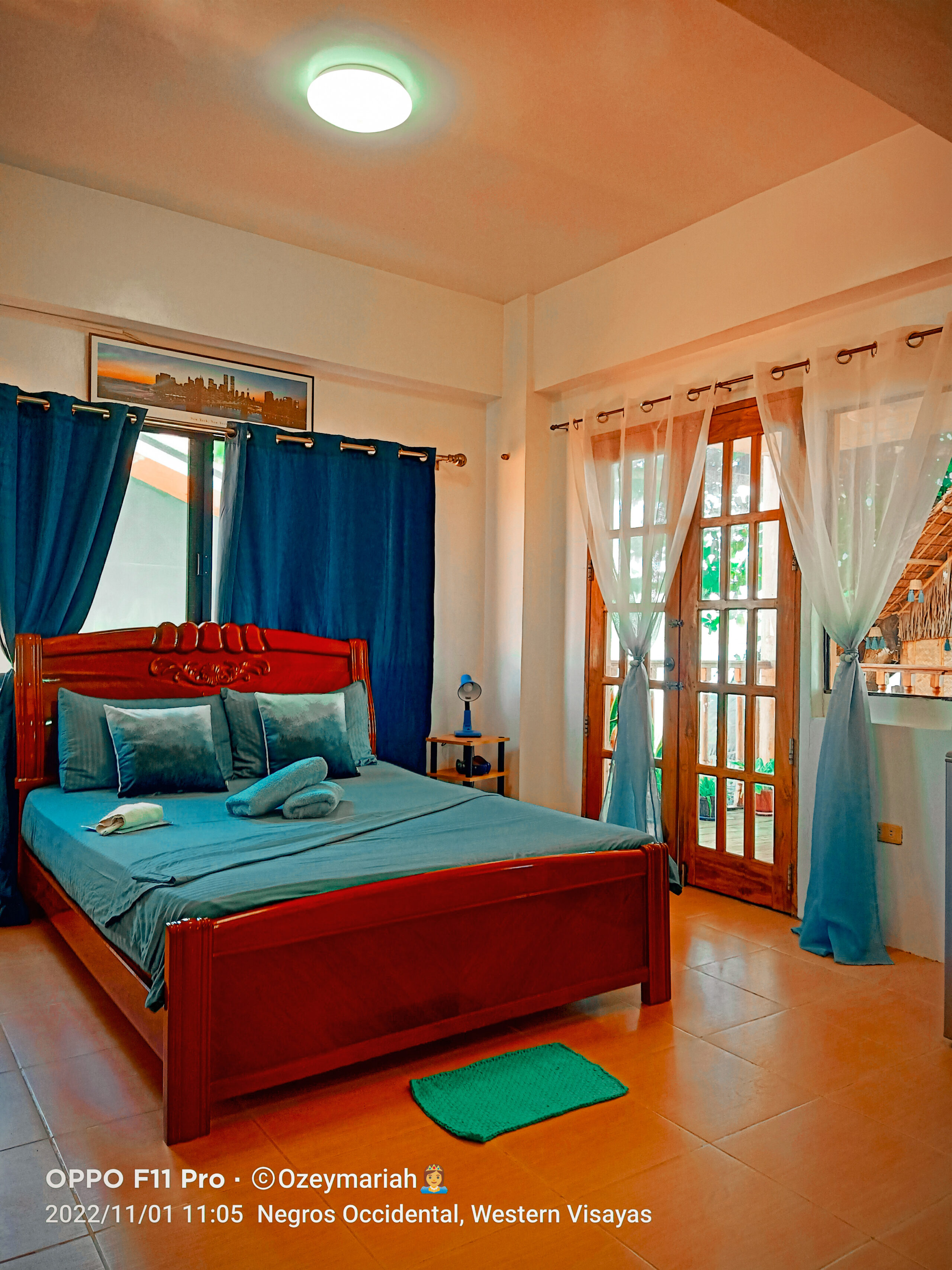 Opposite angle view of the comfortable queen bed, vibrant blue decor, and woodgrain balcony doors in the VIP Executive Suite San Carlos resort.