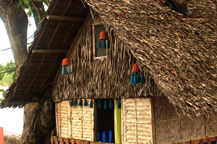 Authentic exterior of the Affordable Treehouse Room San Carlos, showing a tree branch growing right through the traditional nipa rooftop.