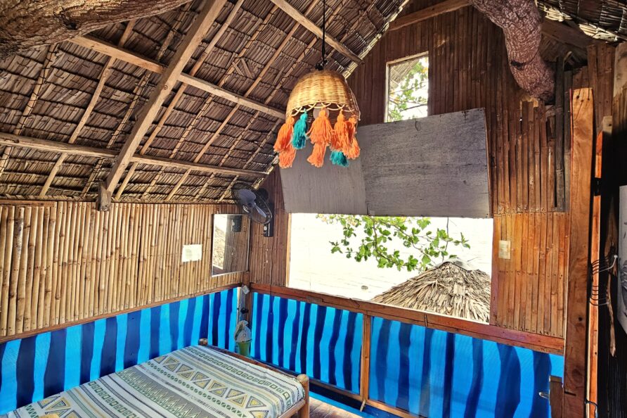 Interior view of the Affordable Treehouse Room San Carlos, showing the bed, wood floor, and elevated sea view out the window.