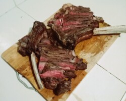 The Chef’s Feature: The Tomahawk Steak. Witness the quality on the grill! Our commitment to professionally managed F&B starts with the best cuts, expertly grilled over an open flame. Tomahawk steak on barbeque with flames at Papa Doug's Steak and Grill