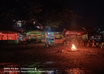 Night campfire on beach with beautifully lit seaside cottages for family reunion venue bacolod