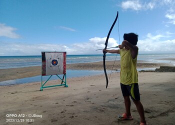 Young boy shooting archery target during family reunion group activities at beach resort