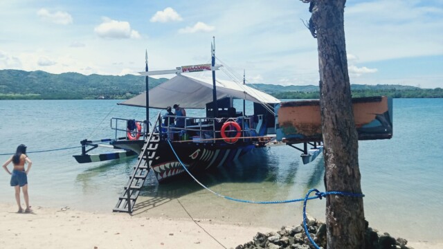 Relaxation Awaits: Spend the afternoon on the white sands of Tiningisan Island, easily accessible via our large party boat! Party boat beached on Tiningisan Island beach